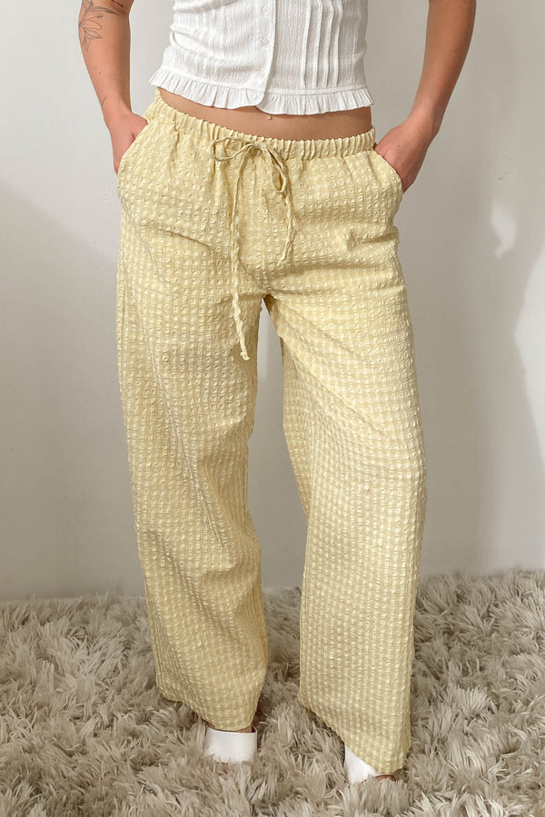Person wearing yellow checkered pants on a textured surface with a neutral background