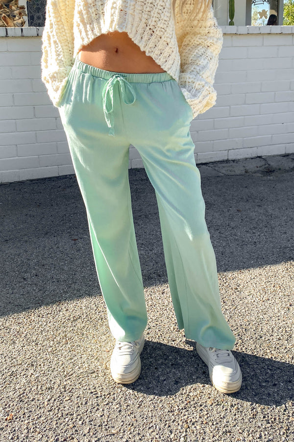 Person wearing light green pants and a beige sweater standing on a street.
