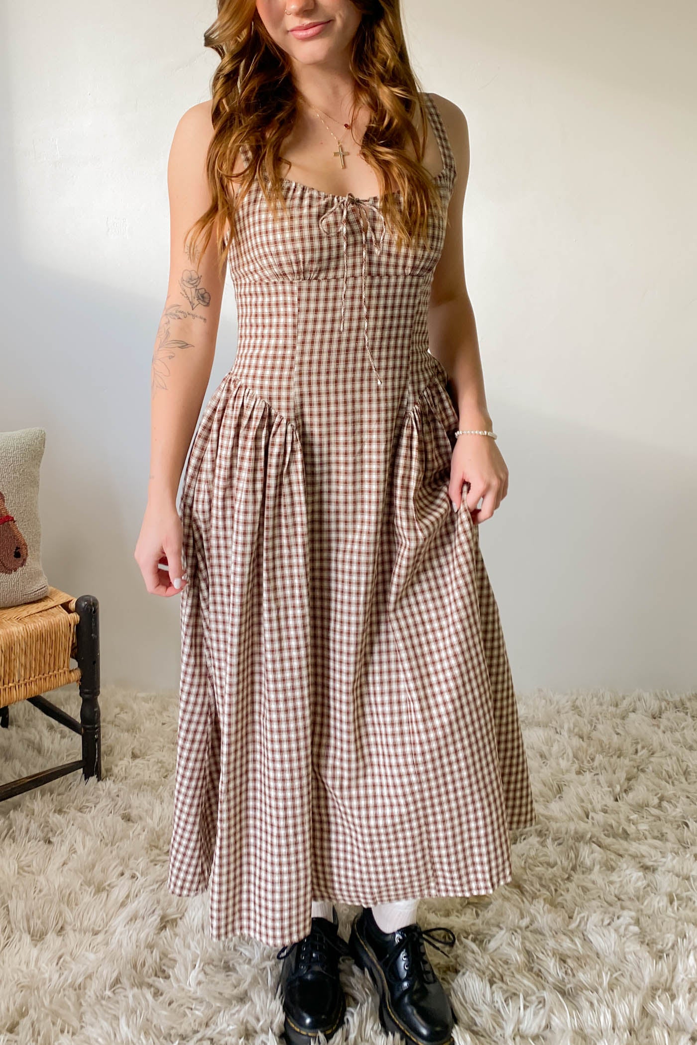 Woman wearing a checkered dress standing in a room with a neutral background